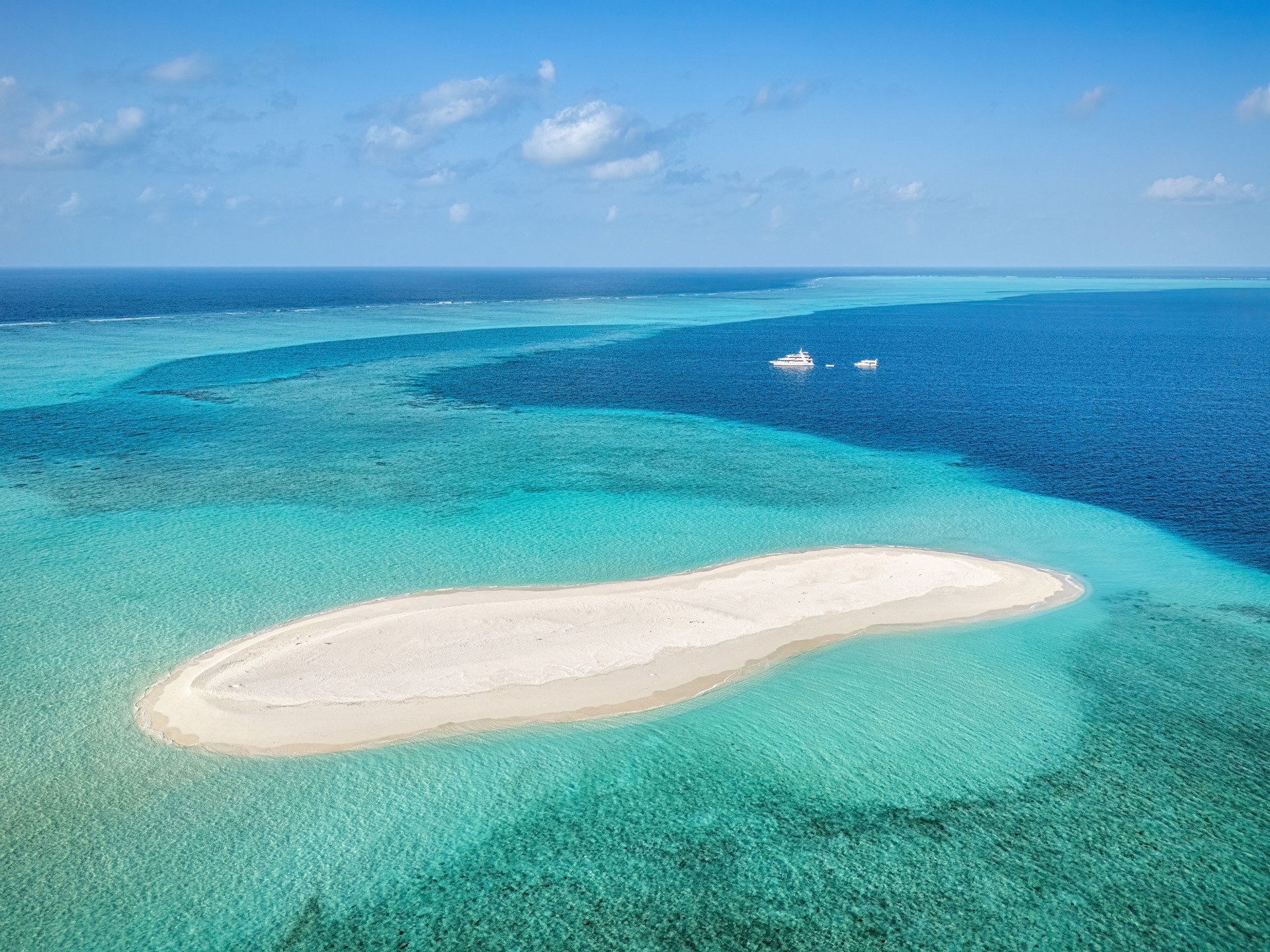 Aerial view revealing sandy bank amid turquoise waters, surrounding luxury yachts highlighting Maldivian seascape's pristine maritime landscape