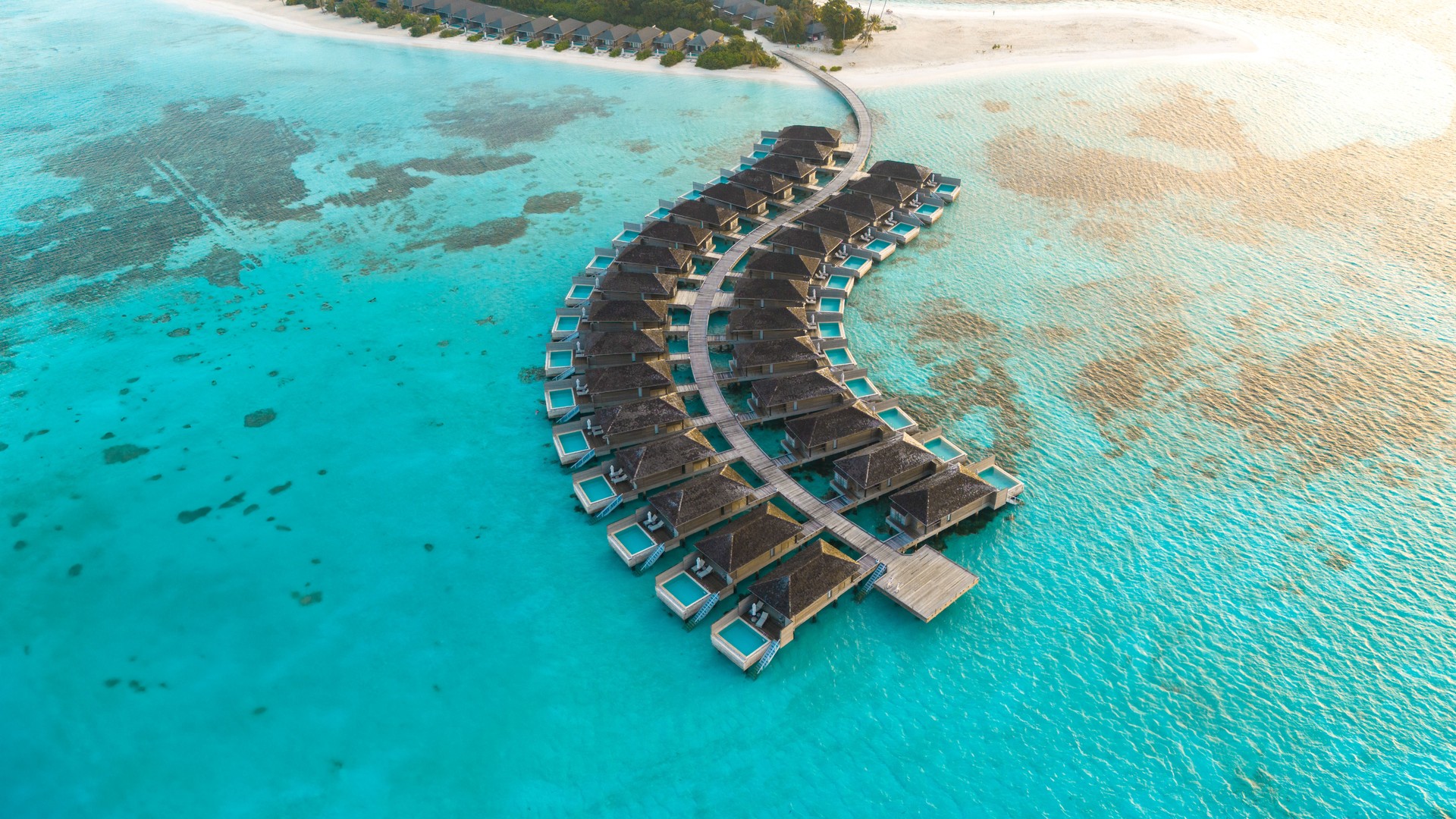 Drone view of Maldives luxury resort with palm trees and ocean villas.